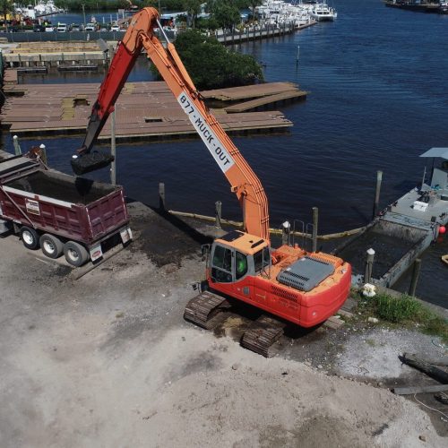 Aerial view of a coastal area with clear blue water and sandy shores, showing a mix of natural landscape and human activity.