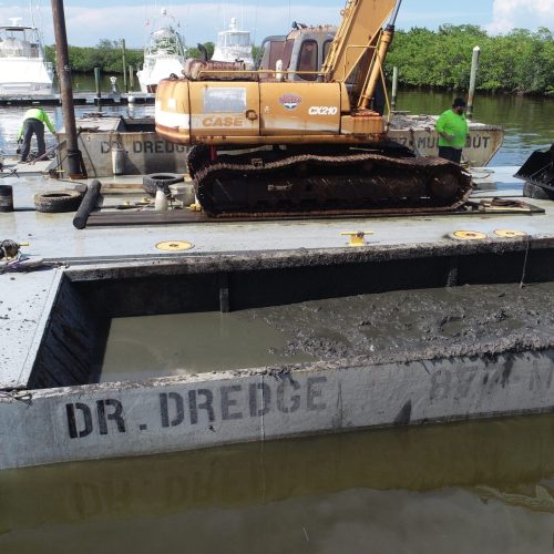 Aerial view of a coastal area with a dredging operation in progress, showing machinery and sediment movement in the water.