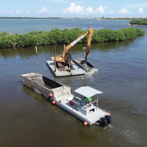 Aerial view of a coastal area with a dredging operation, showing machinery and sediment movement in the water.