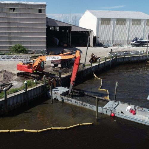 A scenic view of a coastal landscape with calm waters and a clear blue sky, featuring a rocky shoreline and distant hills.