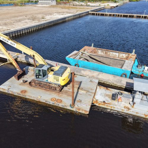 Aerial view of a coastal area with clear blue water and sandy beaches, surrounded by lush greenery and scattered buildings.