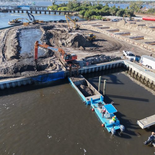 Aerial view of a serene coastline with clear blue waters and a sandy beach, surrounded by lush greenery and distant hills.